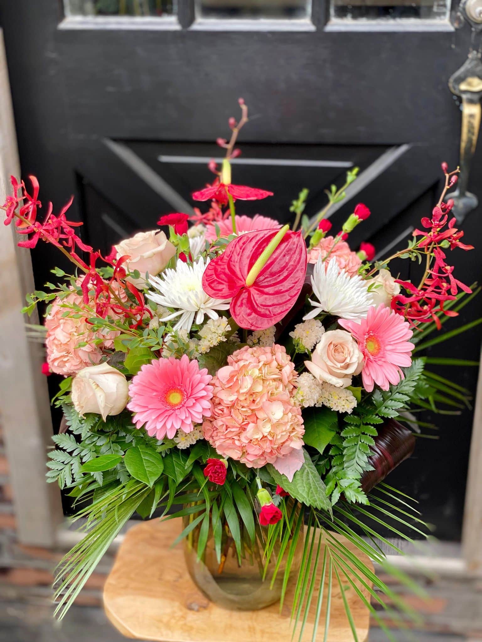 The Watering Can | A large monochramtic bouquet in vase ranging from white, through blush to deep reds on a small side table.