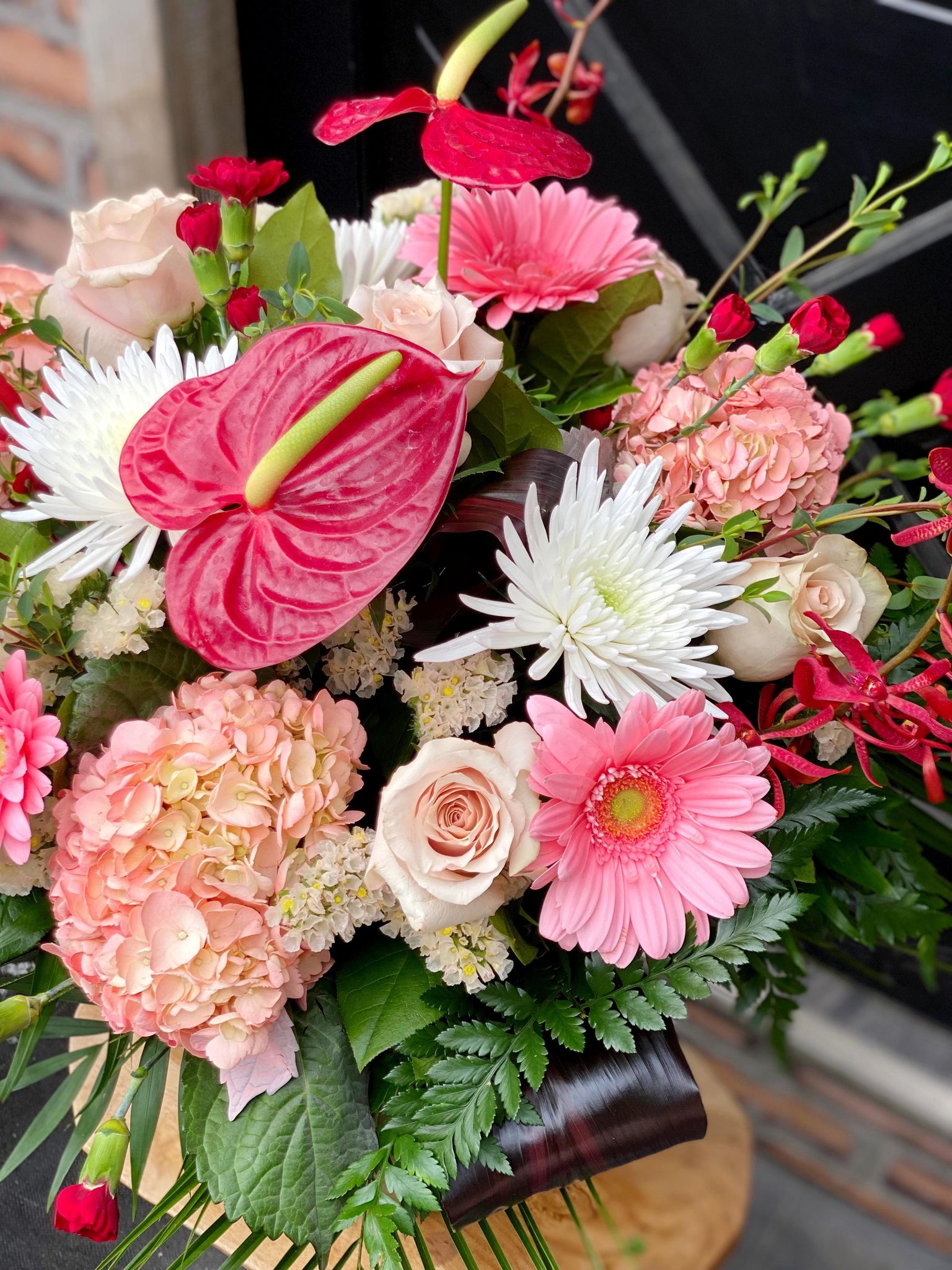 The Watering Can | A close up photo of the flowers in a large monochramtic bouquet in vase with a variety of flowers from white, through blush to deep reds.