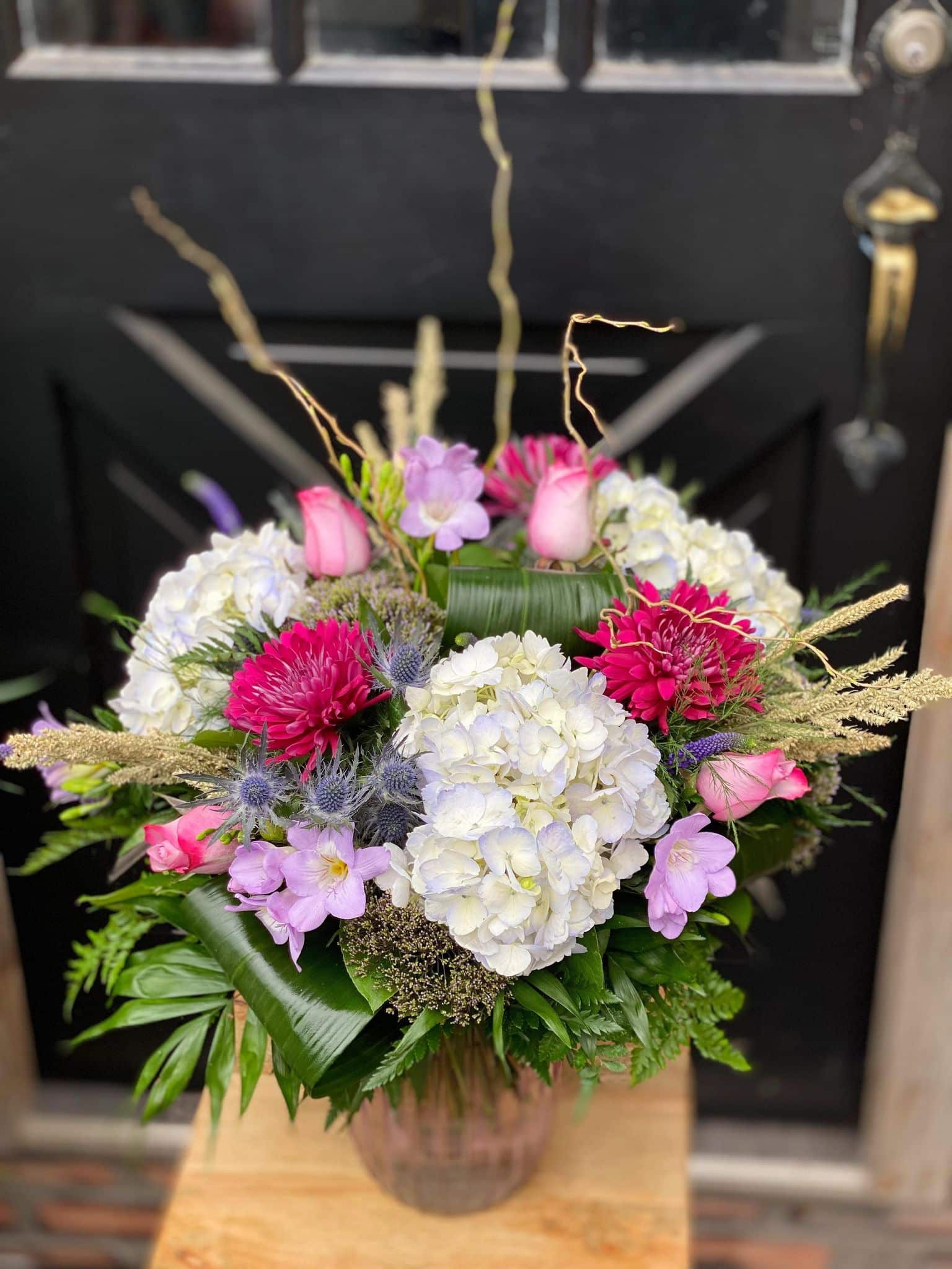 The Watering Can | A large pale blue, ppink and purple bouquet in a tall glass vase.