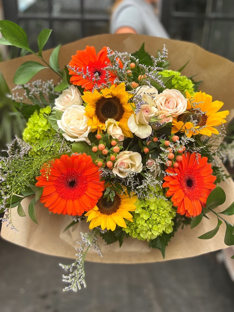 The Watering Can | A summery hand-tied bouquet with sunflowers, orange gerbera daisies and green hydrangea.