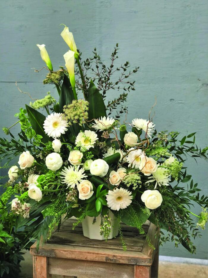 The Watering Can | An asymetrical white side spray with calla lilies, gerberas, roses, mums, rununculus, bells of Ireland, queen Anne's lace, waxflower, curly willow, and a mix of greens.