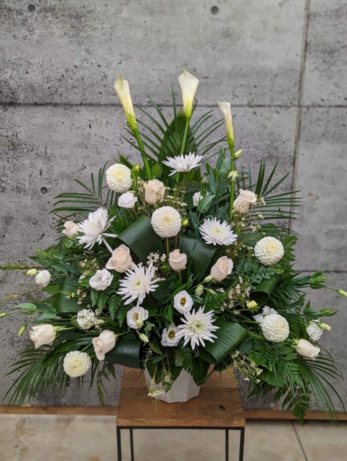 The Watering Can | An all white side spray made with calla lilies, dahlias, roses, waxflower, lisianthus, and mums backed by greens.