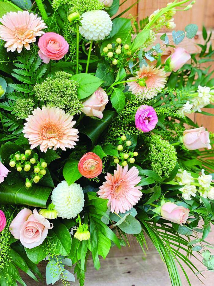 The Watering Can | Close up of peach gerberas, runuclus soft pink roses, white hypericum, and white dahlias in a side spray.