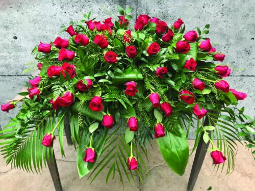 The Watering Can | A casket spray made with red roses and a variety of lush greens.