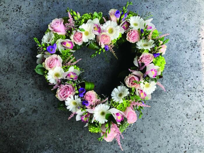 The Watering Can | An open heart design with green hydrangea, soft pink roses, white cymbidium orchids, soft pink astilbe, white mini gerberas, purple freesia, and purple limonium nestled among eucalyptus.