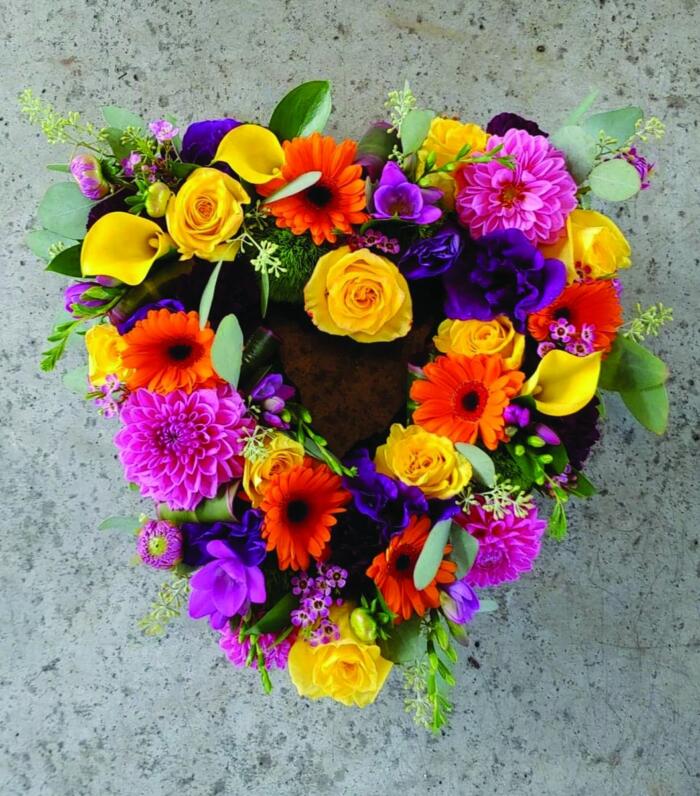 The Watering Can | A small colourful open heart full of yellow roses, pink dahlias, orange gerbera daisies, pink lisianthus, yellow calla lilies, hot pink freesia, dianthus, and hot pink waxflower.