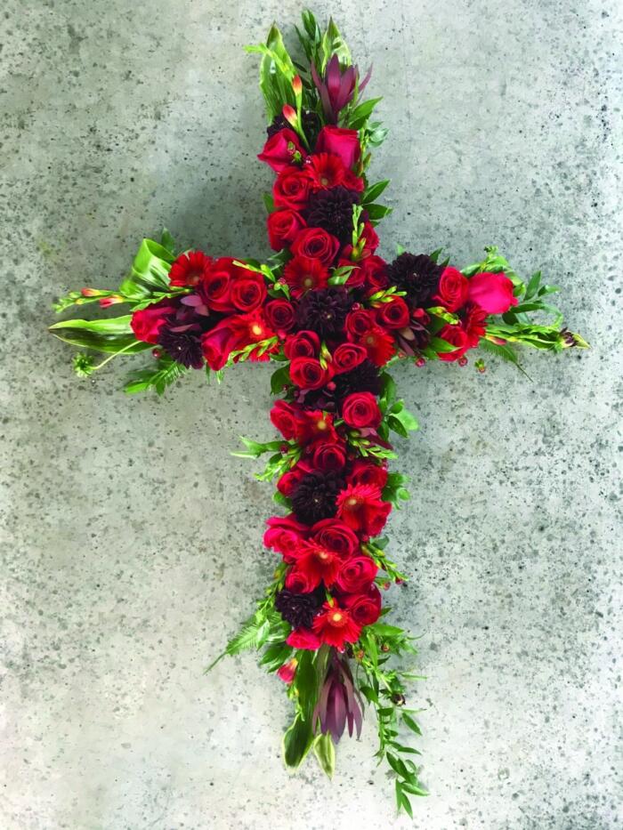 The Watering Can | A red cross shaped floral arrangment featuring roses and dahlias.