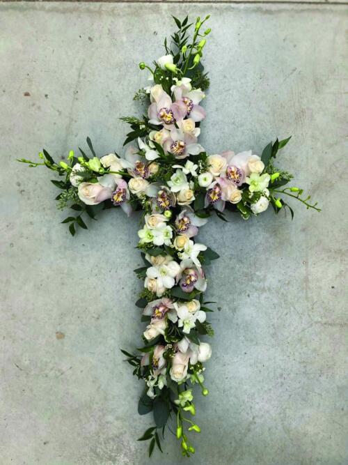 The Watering Can | A soft pink and white flowered cross featuring cymbidium orchids, debdrobium rochids, roses, and ranunuculus.