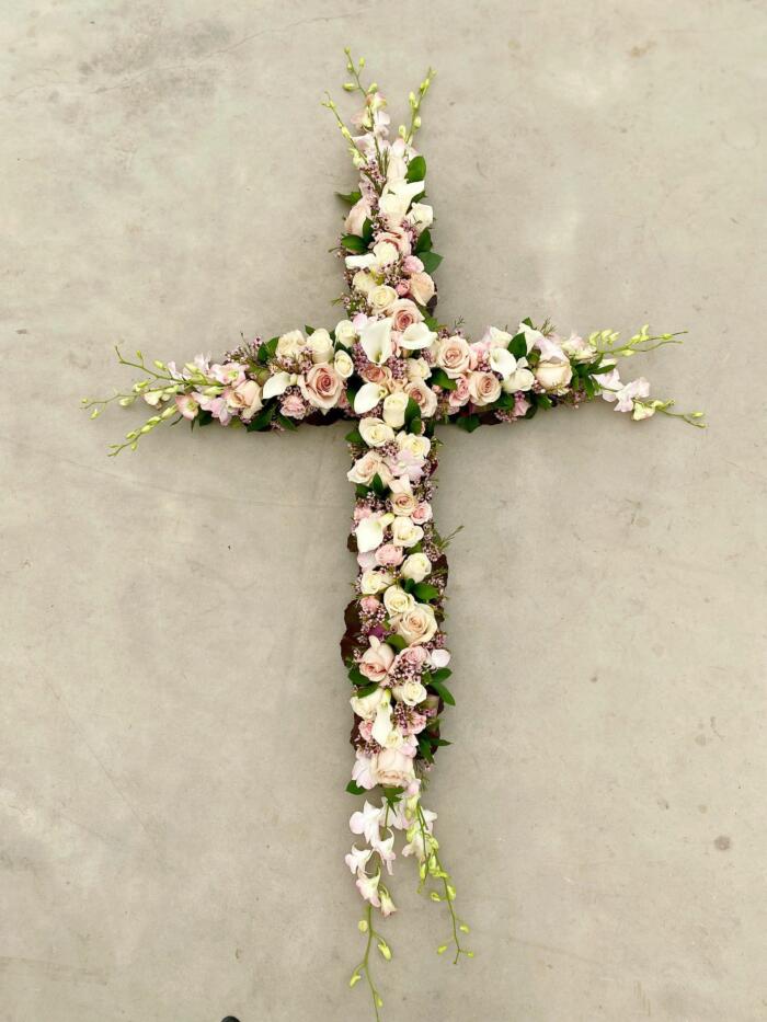 The Watering Can | A large soft pink and white flowered cross featuring roses, cymbidium orchids, dendrobium orchids, and calla lilies.