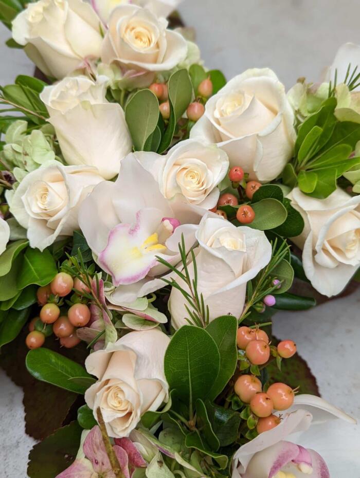 The Watering Can | Close up of white roses, white cymbidium orchids. and peach hypericum in a floral cross.