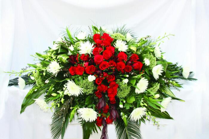 The Watering Can | A rounded green and white casket spray with a cross of red flowers acorss the centre.