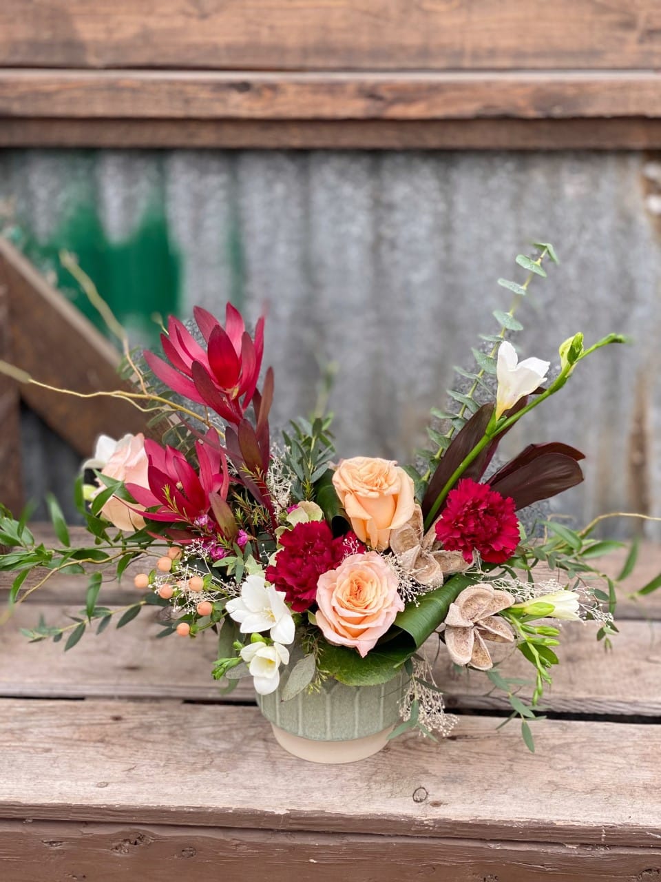 The Watering Can | A red and blush european style floral arrangement that spills in a 'V' shape from a green ribbed ceramic container.