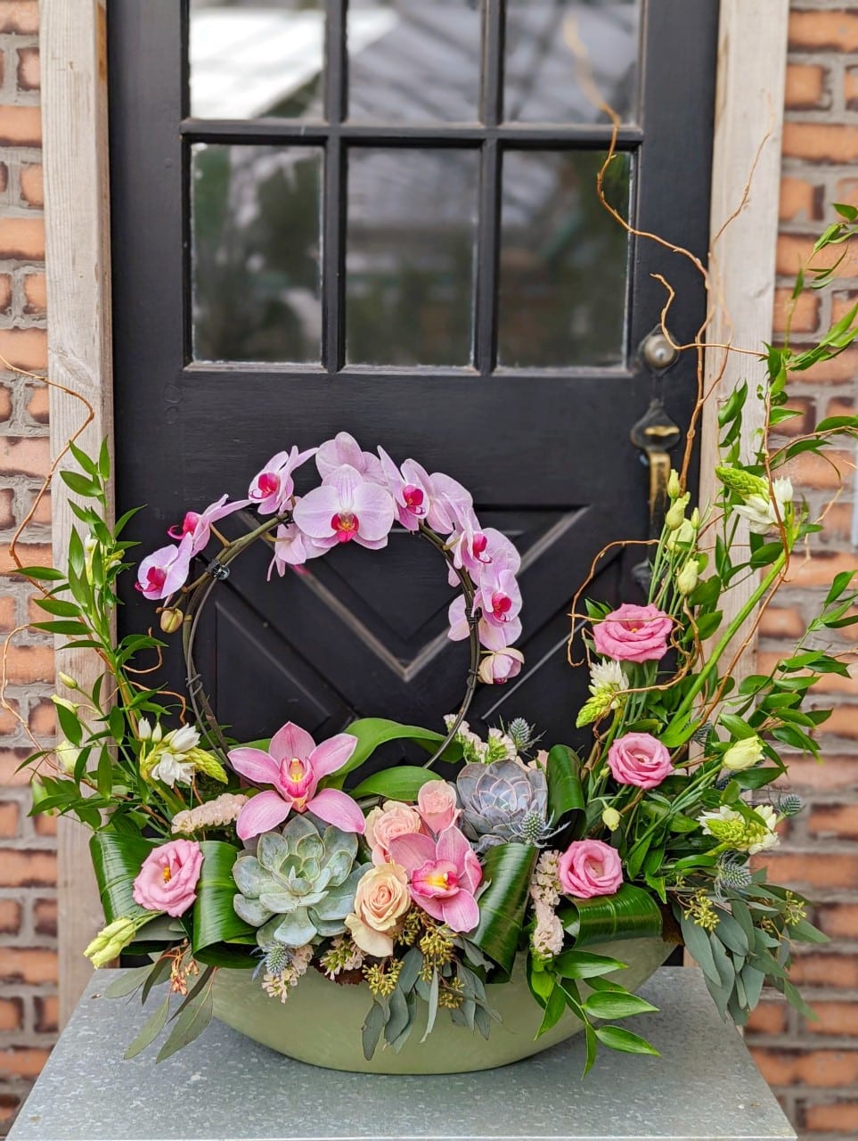 The Watering Can | Pink and green large oblong European style arrangement with lots of orchids.