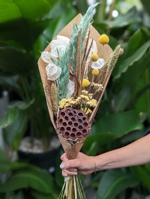 The Watering Can | A bundle of dried flowers in white, seafoam green, and a op of yellow wrapped in brown paper.