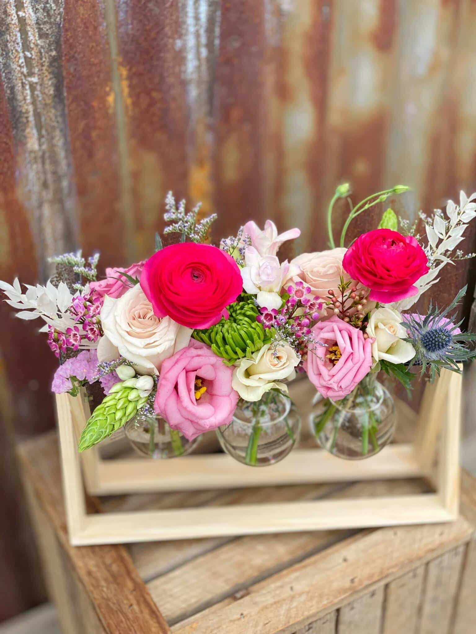 The Watering Can | Pink blooms in a set of 3 glass bud vases suspended from a wooden frame.