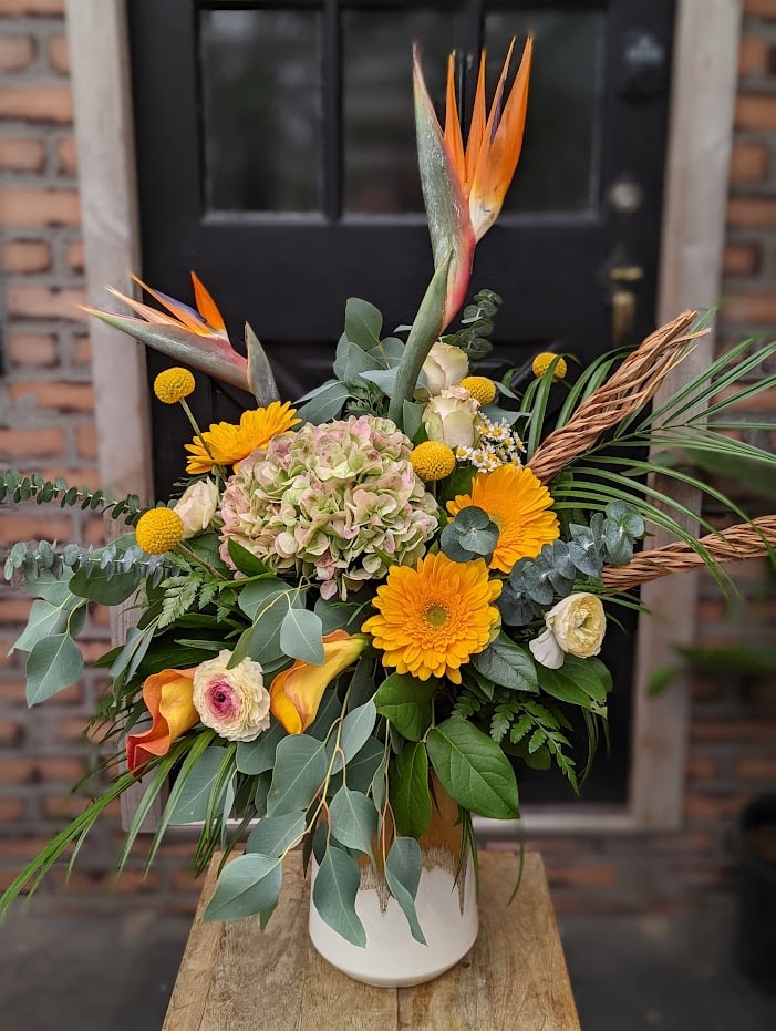 The Watering Can | A large asymmetrical yellow and orange bouquet in a cream, yellow, and brown ceramic vase.