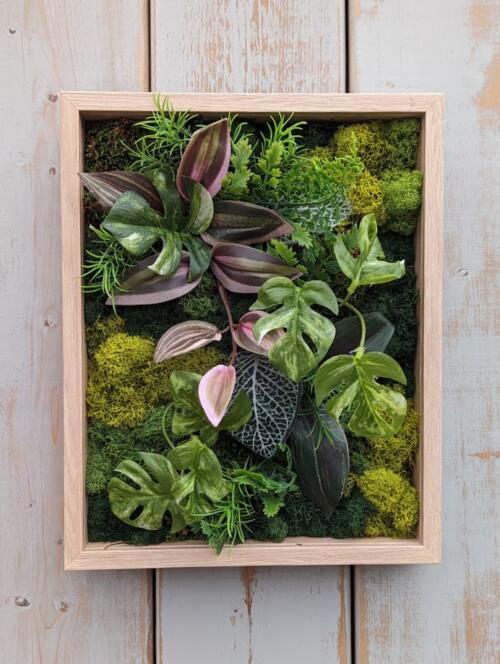 The Watering Can | A lush green moss frame accented with faux tropical foliage in a light wooden frame.